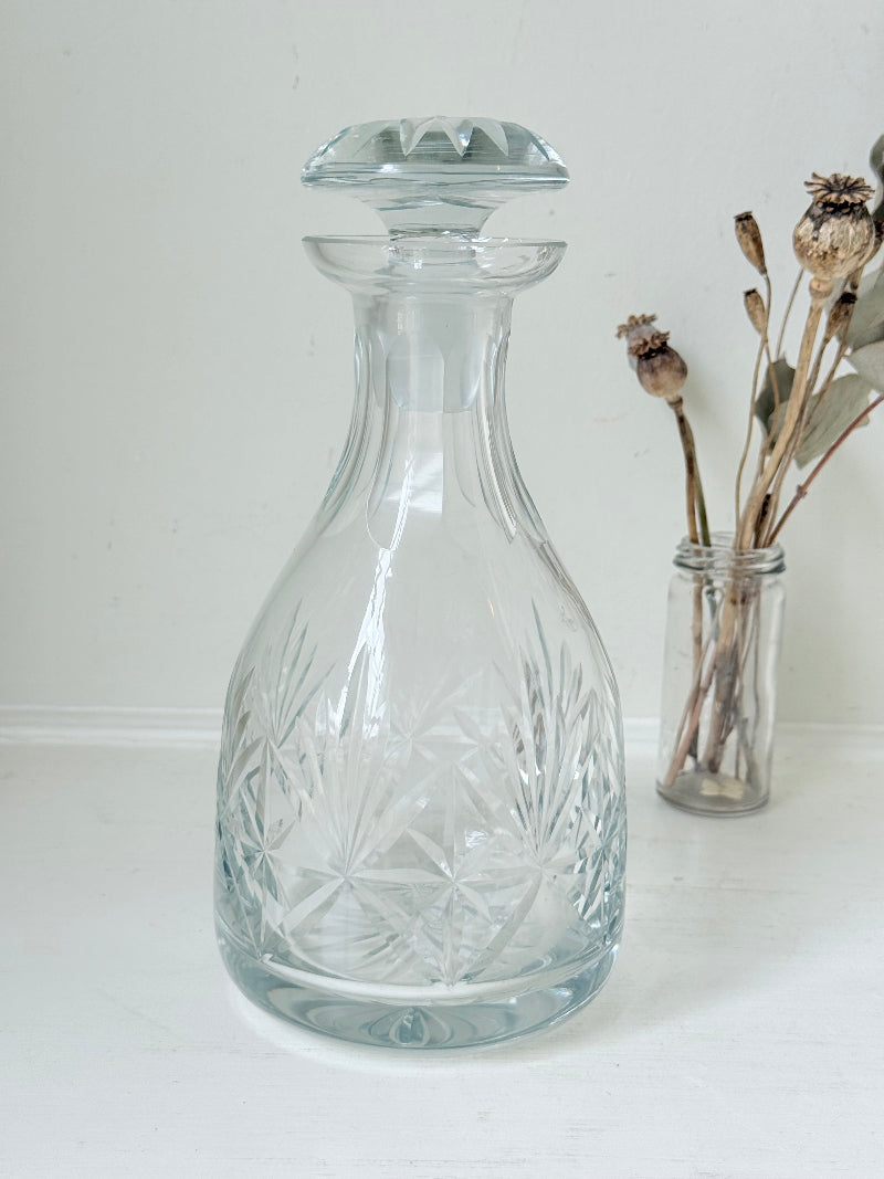 Vintage crystal decanter with faceted stopper and cut glass starburst design, photographed on a white surface