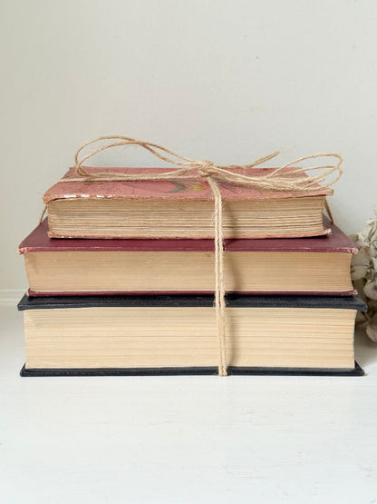 Vintage decorative book bundle in red and black with gilt detailing tied with twine, photographed on a white surface