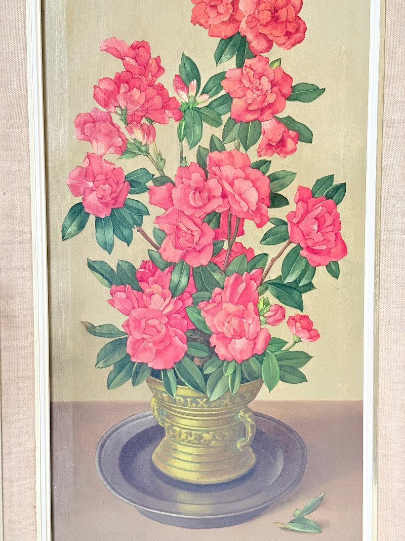 A framed botanical painting of vibrant pink flowers with green leaves arranged in a gold-colored vase on a dark round tray, set against a light beige background.