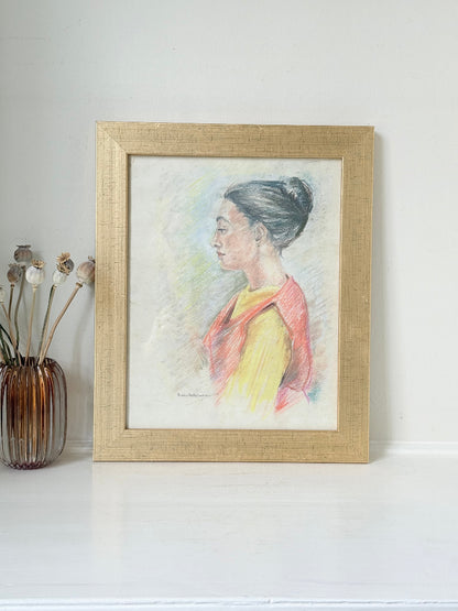 Vintage pastel portrait of a woman in profile wearing red and yellow, framed under glass, photographed on a white surface
