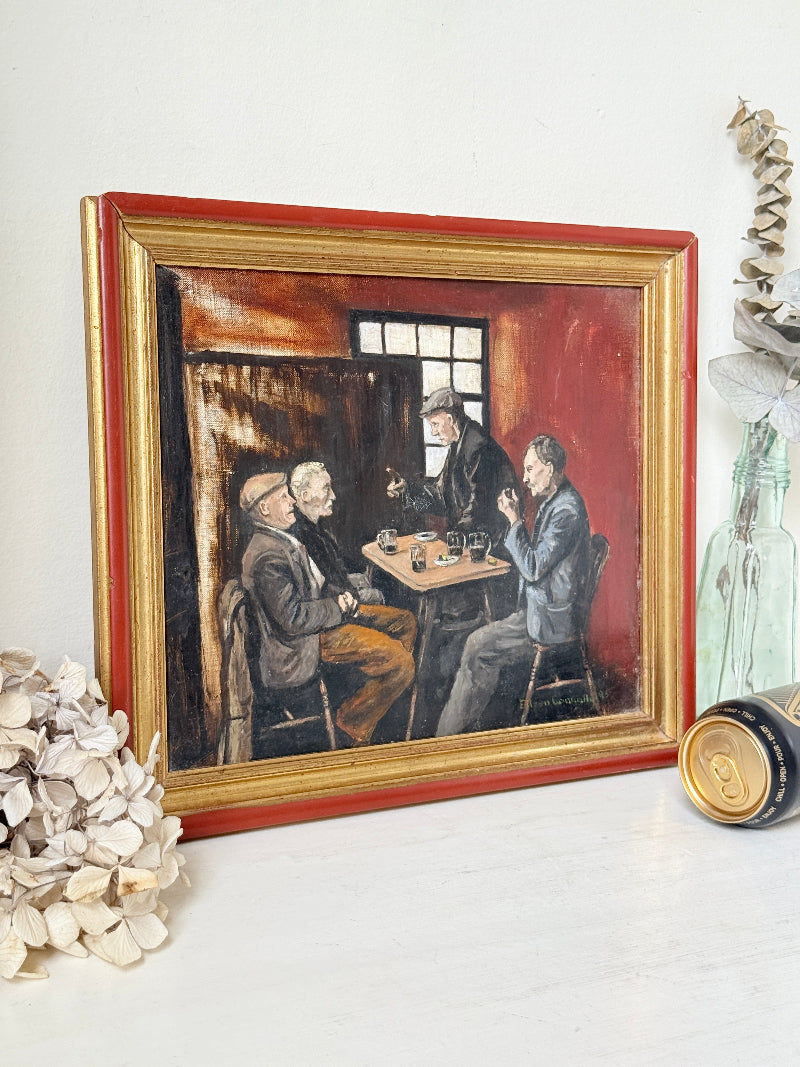 A framed oil painting depicting three men in suits sitting around a table, displayed on a white surface with dried flowers and decorative props.