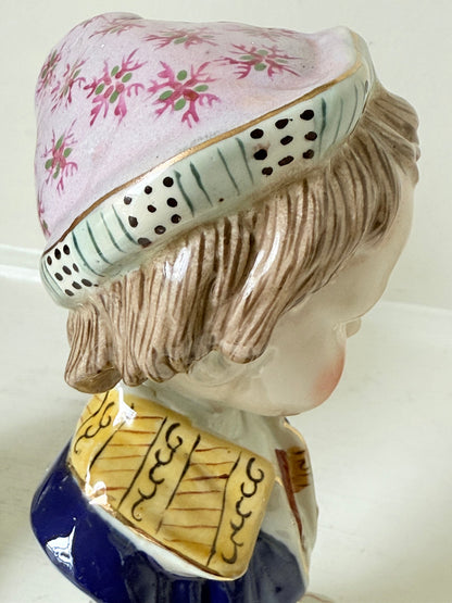 Hand painted Victorian Staffordshire ceramic children busts on white surface, photographed beside dried stems.
