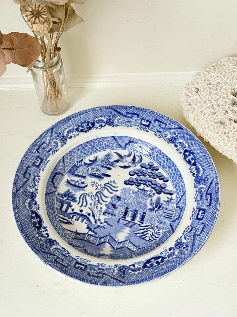 Antique Blue Willow serving bowl with cobalt transfer pattern shown on a white surface.