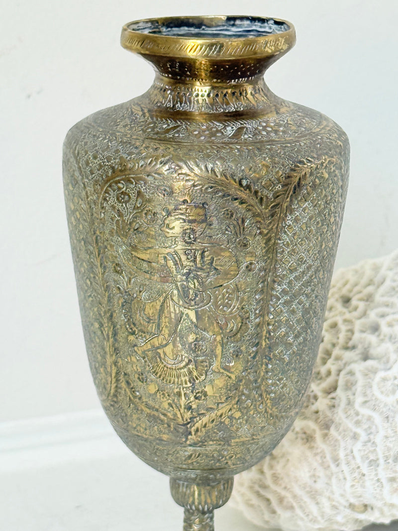 Indian Benares brass chalice vase with figural panels and pedestal base, photographed on a white surface