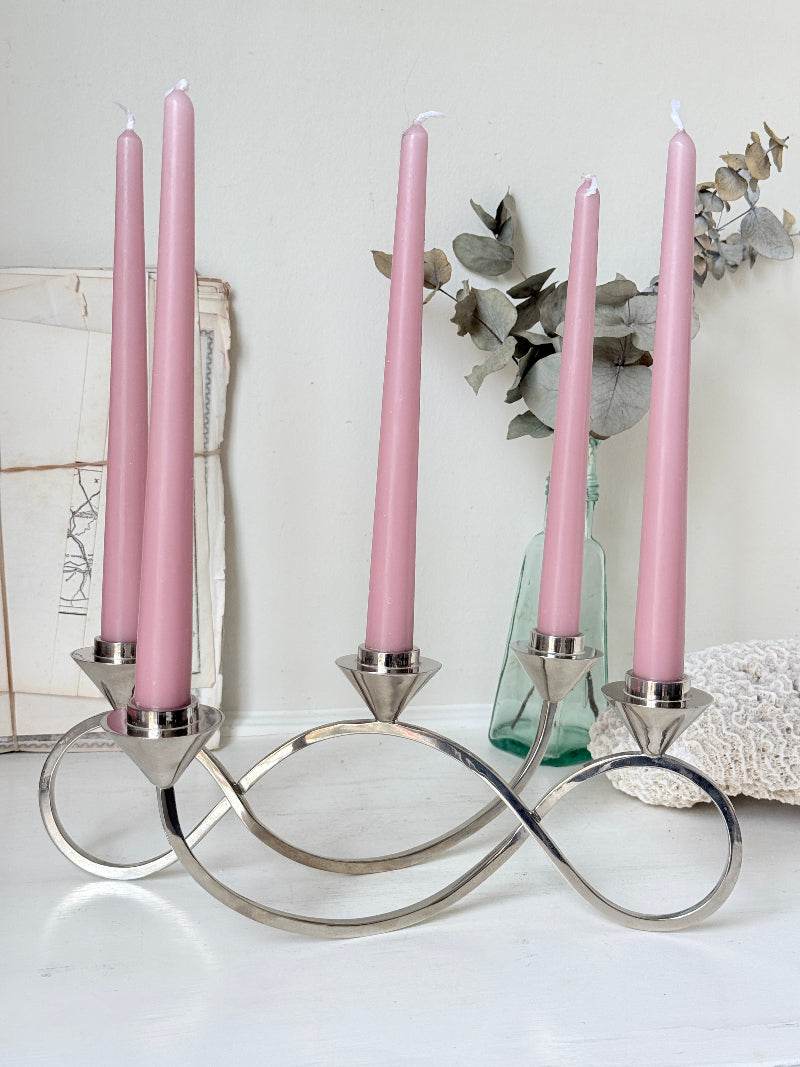 Silver tone five light candelabra with a sculptural looped base holding pink candles, photographed on a white surface