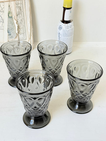 Set of four smoke grey pressed glass footed goblets with a diamond pattern, photographed on a white surface