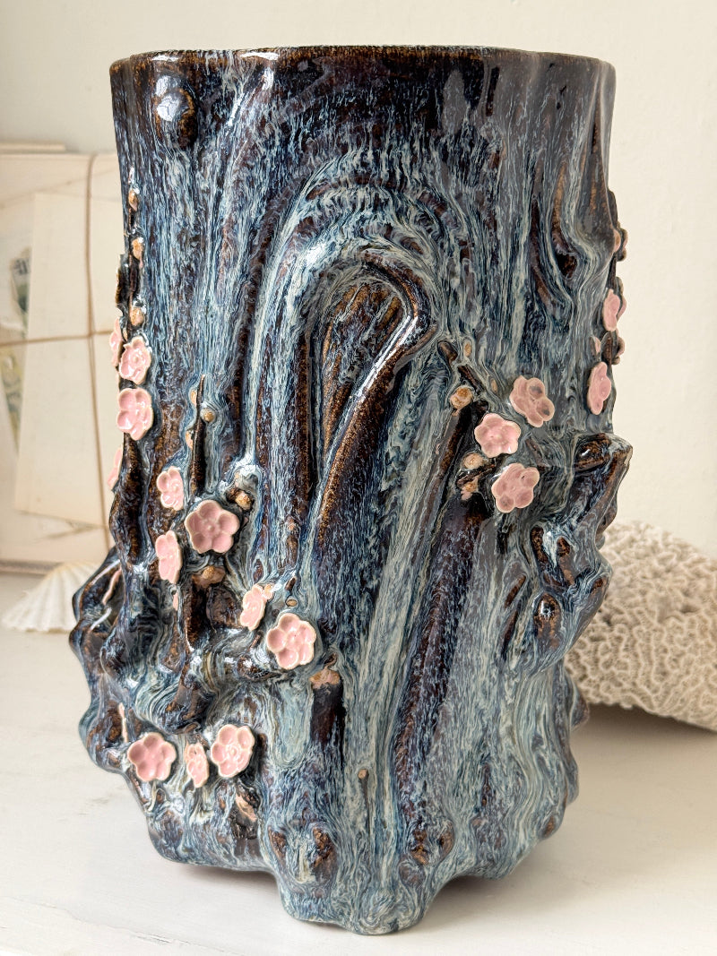 Large ceramic tree trunk vase with applied pink cherry blossom detail, textured bark form and dark drip glaze