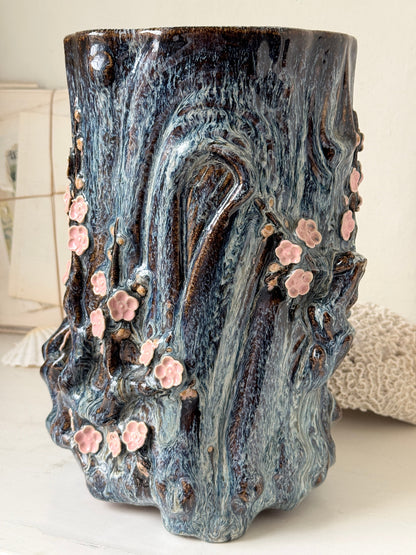 Large ceramic tree trunk vase with applied pink cherry blossom detail, textured bark form and dark drip glaze