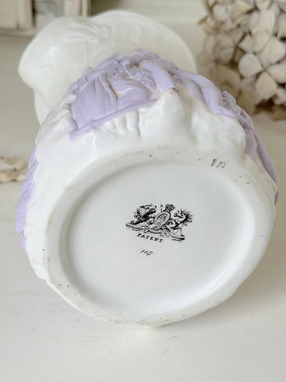 Close-up of the base of a vintage white ceramic pitcher or vase with pale lavender relief decoration and a black patent mark reading &