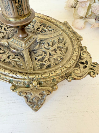 Ornate vintage brass candlestick with decorative handle and footed base, photographed on a white surface