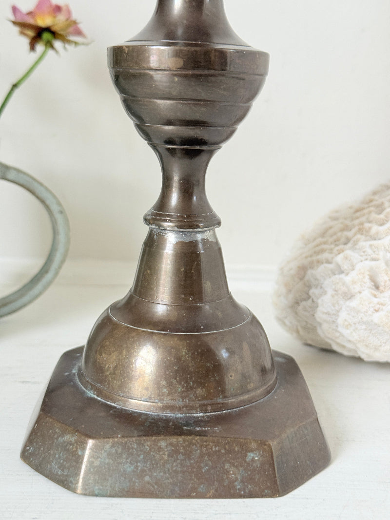 Bronze coloured vintage candlestick with bobbin stem and shaped base styled with taper candle on white surface