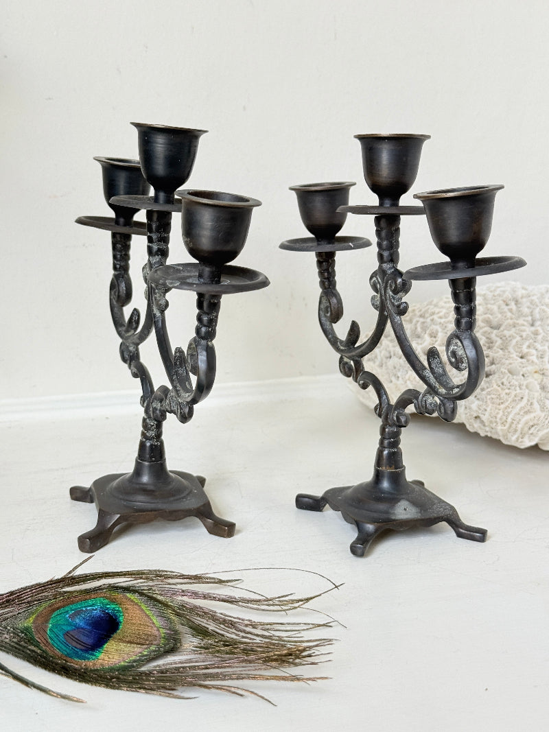Pair of vintage brass three arm candelabra with scrolling arms and aged patina, photographed on a white surface