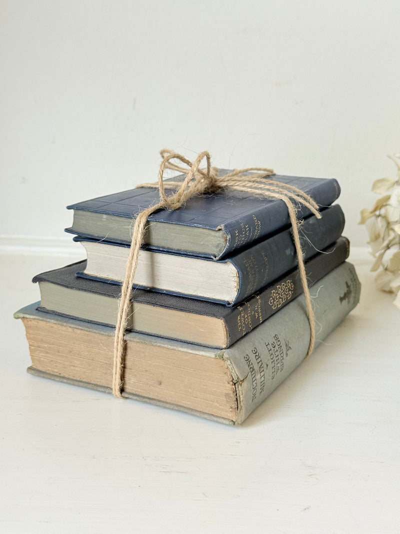 Vintage decorative book bundle in navy, grey, and cream tied with twine, photographed on a white surface