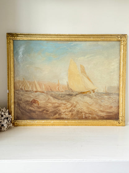 An oil painting of a sailing race on the sea, housed in an ornate gold frame, resting on a white shelf against a neutral wall.
