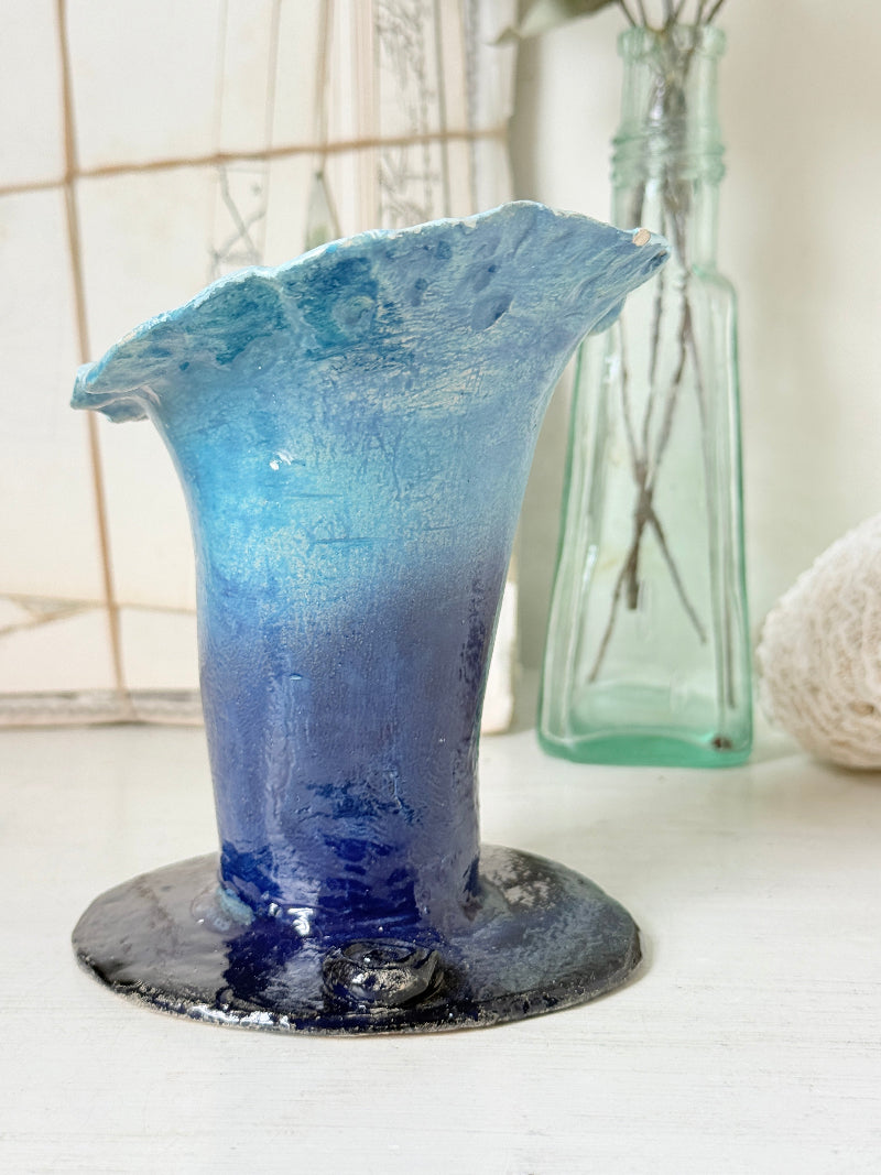 Handmade studio pottery trumpet vase in ombre blue with a frilled rim, photographed on a white surface