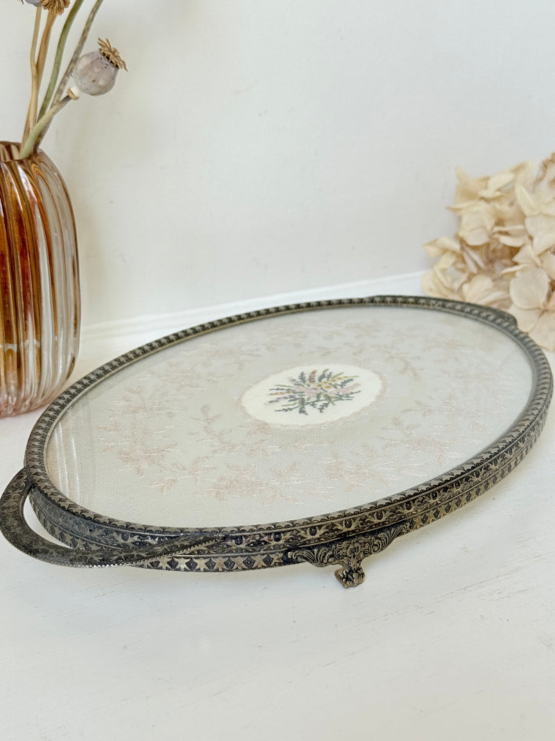 Vintage oval metal tray with pierced gallery sides, twin handles, and floral centre, photographed on white surface.