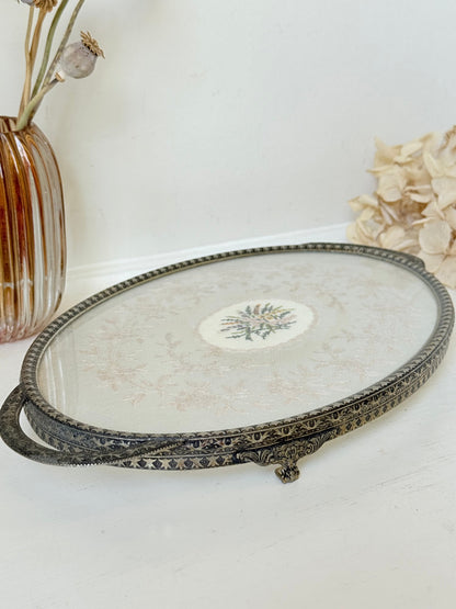 Vintage oval metal tray with pierced gallery sides, twin handles, and floral centre, photographed on white surface.