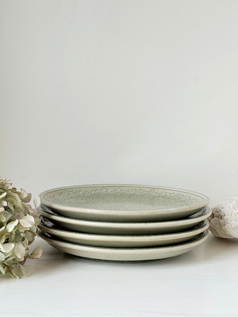 Set of four large Thai celadon stoneware plates in soft green glaze with raised pattern, photographed on a white surface