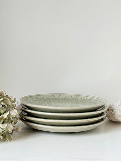 Set of four large Thai celadon stoneware plates in soft green glaze with raised pattern, photographed on a white surface