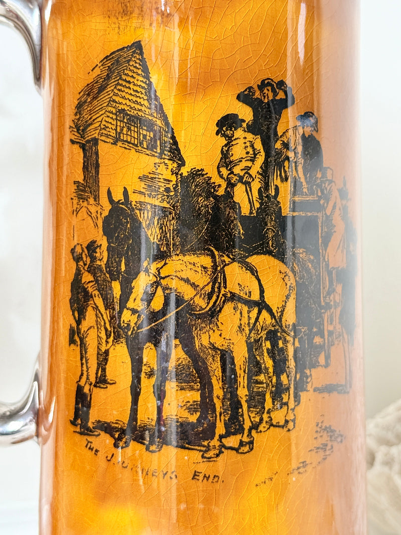 Antique Ridgways stoneware tall jug photographed on a white surface in amber treacle glaze with black transfer scenes and silver tone rim