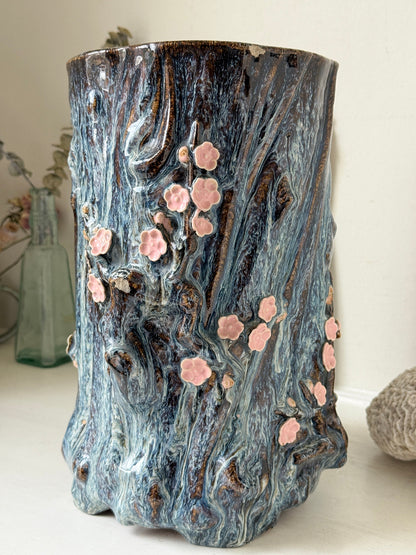 Large ceramic tree trunk vase with applied pink cherry blossom detail, textured bark form and dark drip glaze