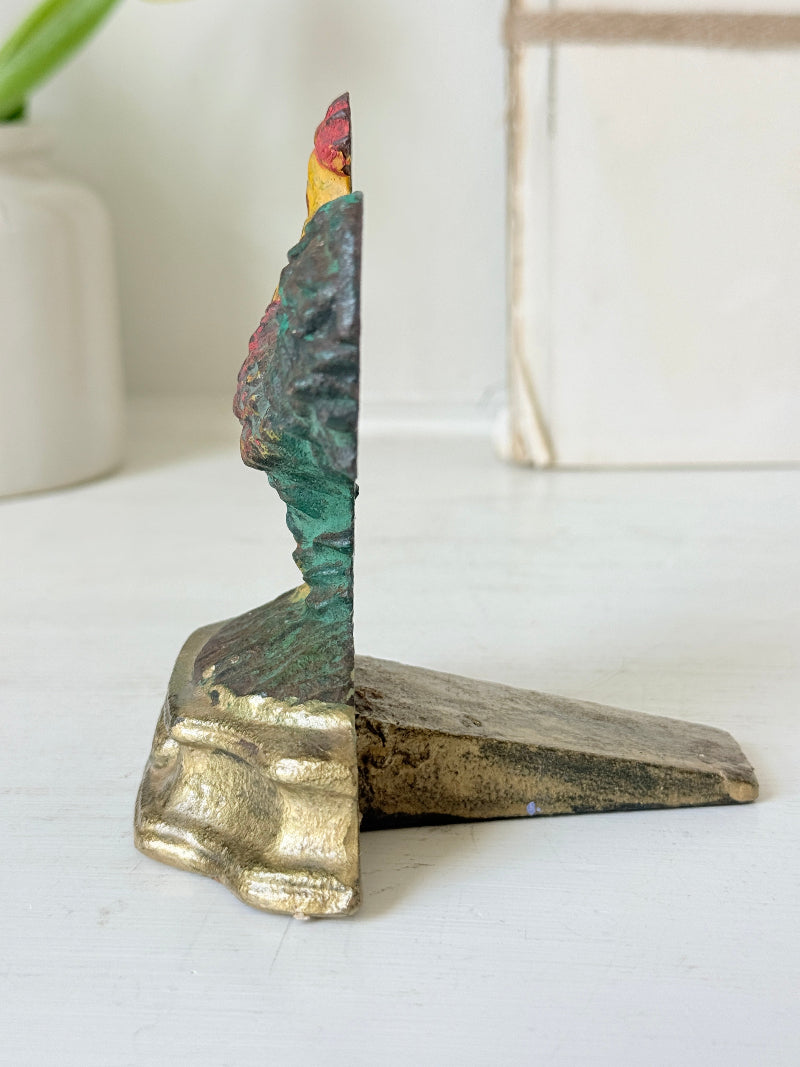 A vintage-style decorative bookend shaped like a stylized tree trunk with a gold-toned base and a textured top featuring green, blue, and red painted details, shown on a white tabletop.