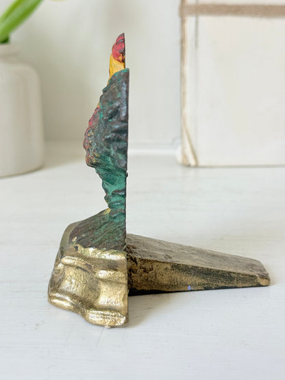 A vintage-style decorative bookend shaped like a stylized tree trunk with a gold-toned base and a textured top featuring green, blue, and red painted details, shown on a white tabletop.