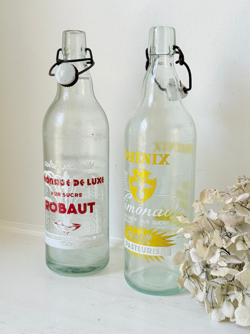Pair of vintage French glass bottles with retro typography and graphics, photographed on a white surface