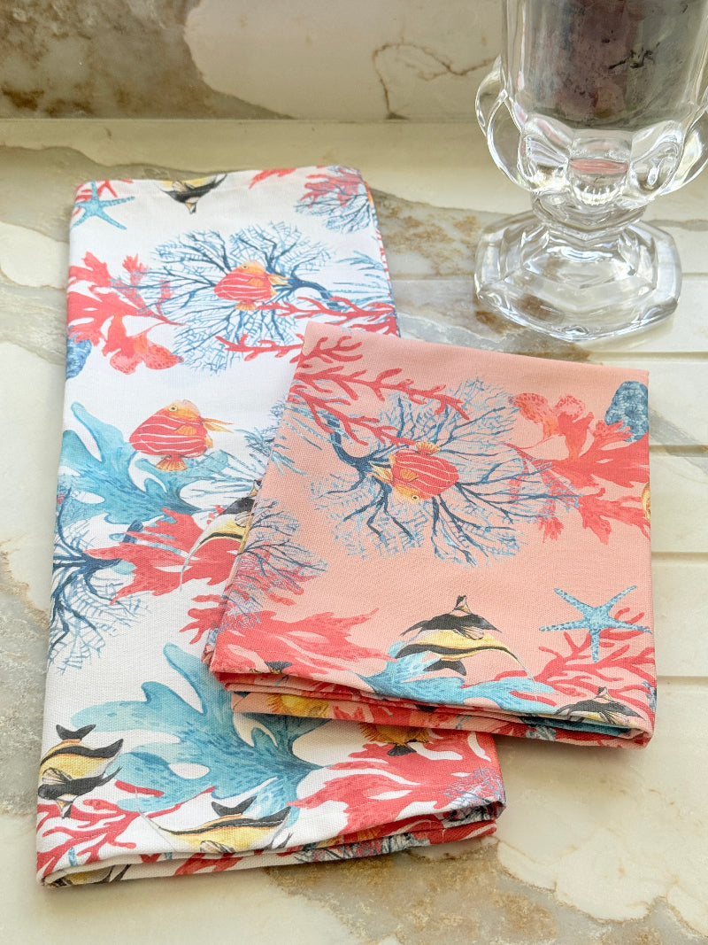 Coral reef print cotton tea towel in crisp white with colourful coral and tropical fish motifs, photographed indoors