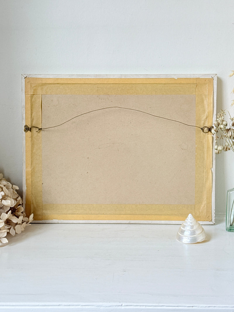 The back of a square picture frame with a light wood border, brown backing board, and hanging wire, displayed on a white surface with decorative dried flowers and a small shell.
