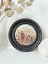 Antique Prattware framed ceramic lid with rural family scene photographed on a white surface.