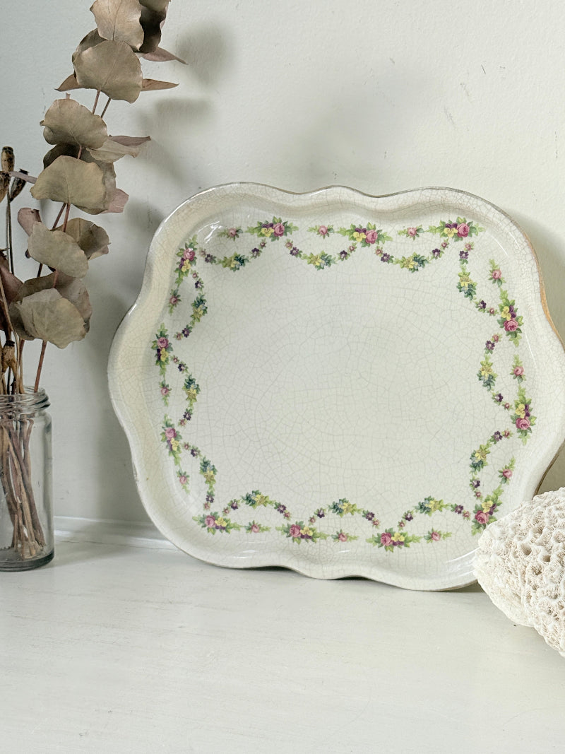 Vintage cream ceramic serving plate with scalloped wavy edge and pink and green floral garland border photographed on a white surface