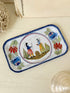 A rectangular white enamel tray with a blue hand-painted border and a central illustration of two figures in traditional clothing, surrounded by floral motifs, displayed on a light wooden surface.