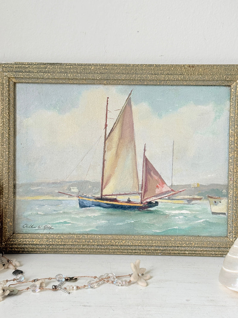 A framed watercolor painting of two sailboats on the sea, housed in an ornate gold frame, displayed on a white surface with decorative jewelry nearby.