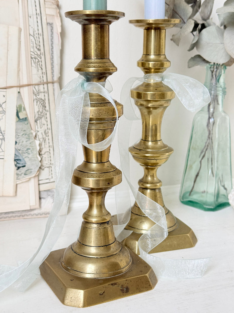 Pair of tall antique brass candlesticks with knopped columns and octagonal stepped bases holding blue and green tapers