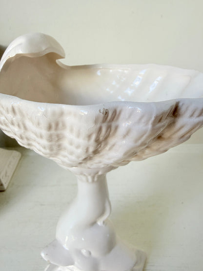 A white ceramic pedestal bowl with a textured, ribbed exterior and a smooth, open interior, shown on a light-colored surface against a neutral background.