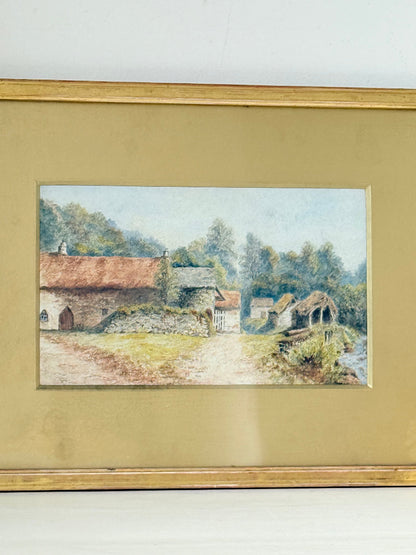 Framed vintage watercolour of countryside farm buildings with red roofs in gold frame photographed on a white surface