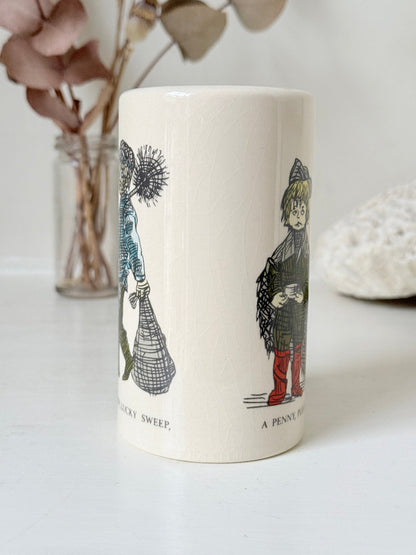 Vintage ceramic money box with illustrated figures photographed on a white surface