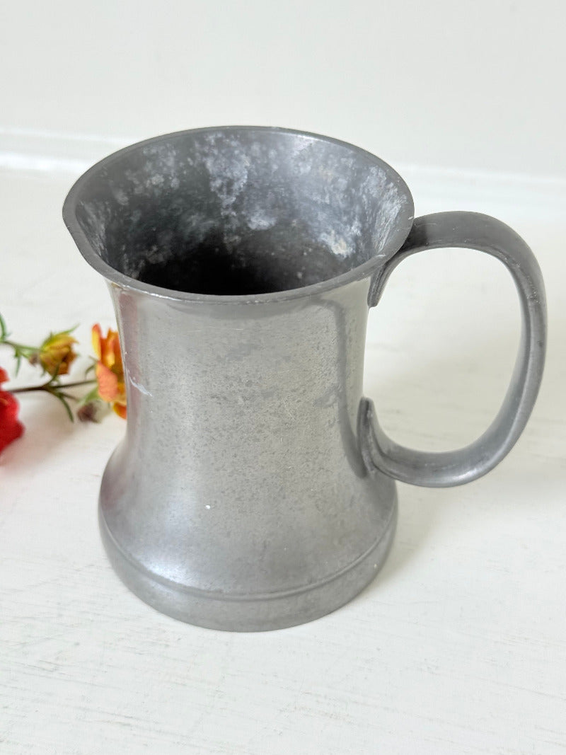 vintage pewter tankard with crown and rose mark and handle, styled with red and orange flowers on white surface