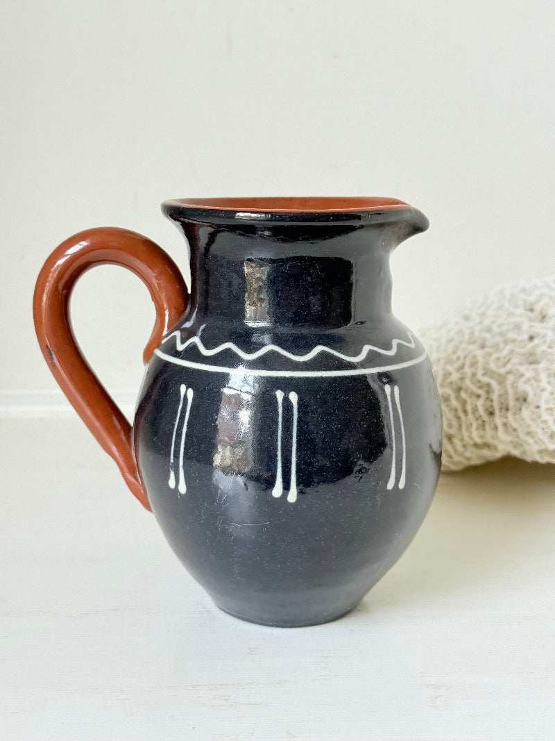 Slipware studio pottery jug with blue glaze and terracotta handle, photographed on a white surface