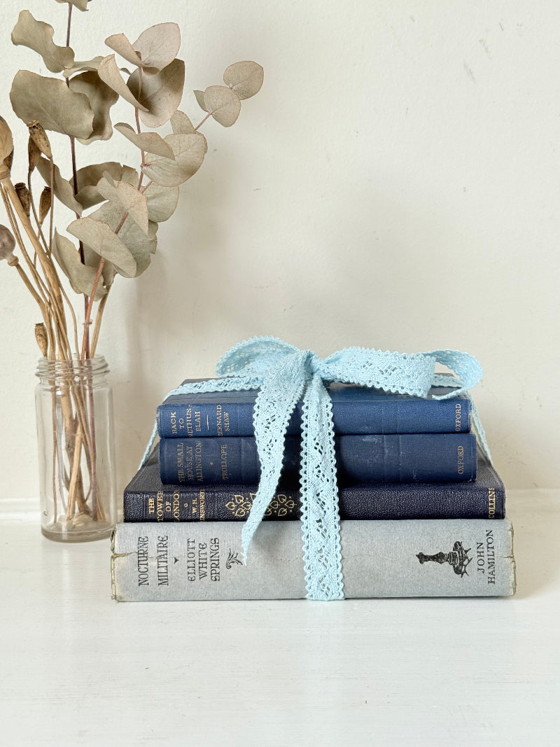 Vintage navy decorative book bundle tied with pale blue lace ribbon, photographed on a white surface
