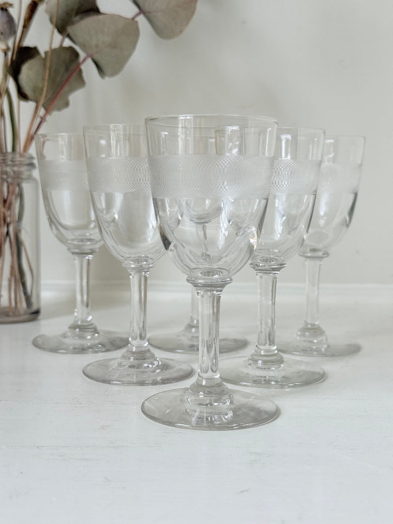 Set of six vintage etched clear glasses with decorative banding, one with a tiny rim chip, photographed on white surface.