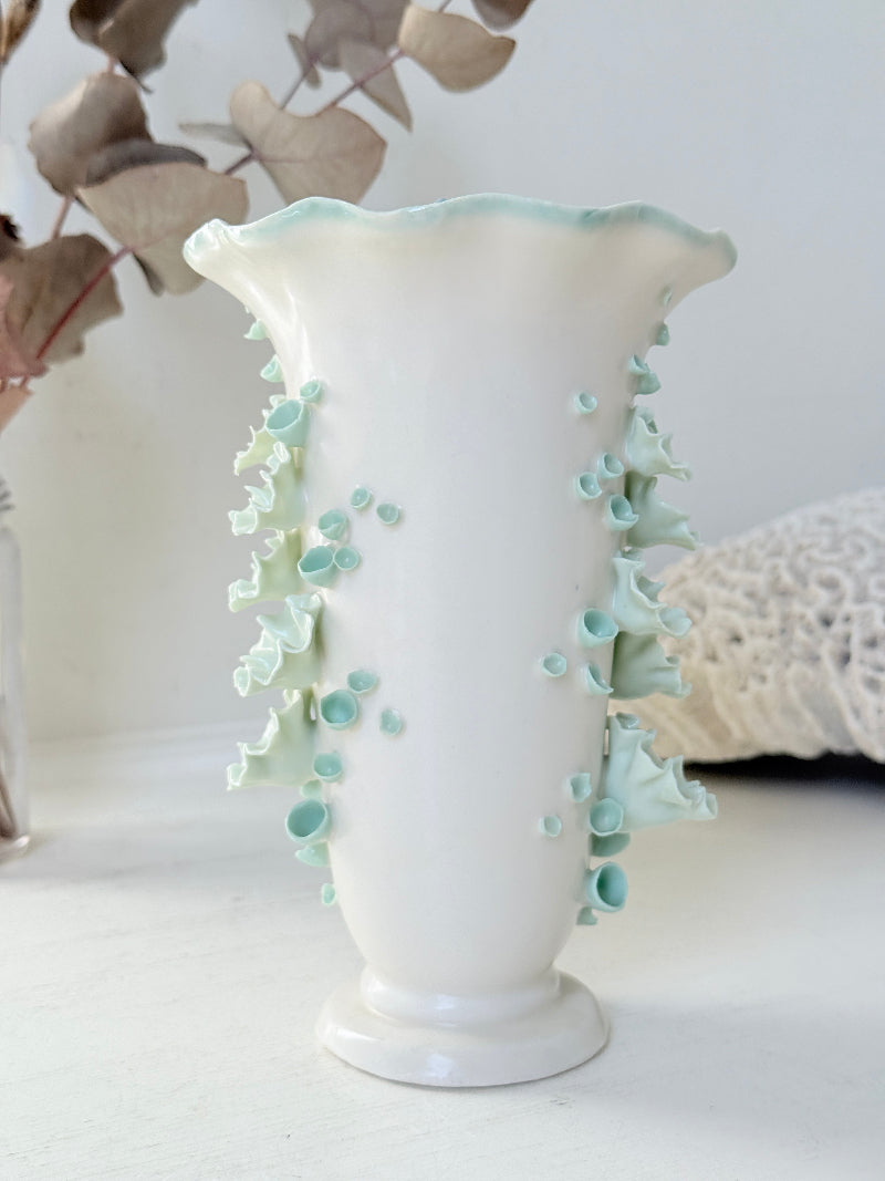 White Chessell Pottery studio vase with rippled rim and raised aqua floral decoration photographed on a white surface