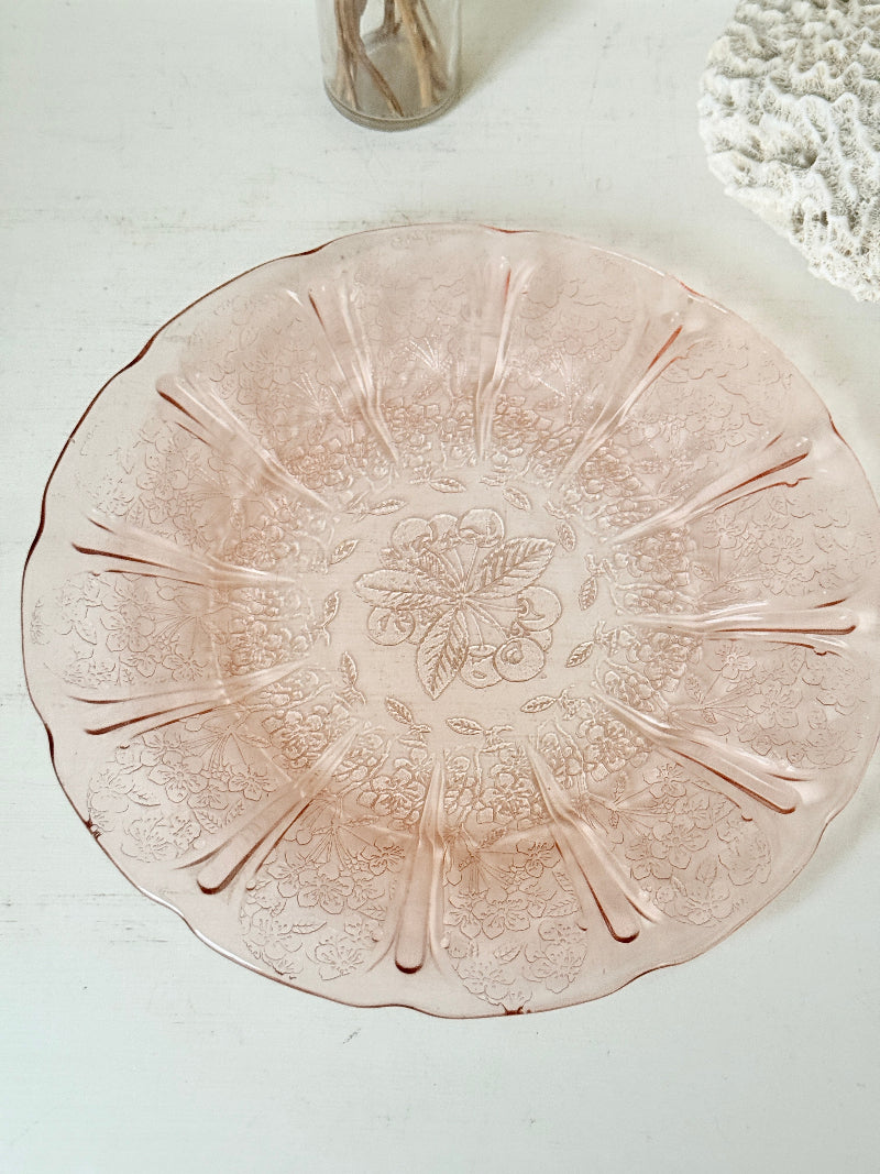 Vintage blush pink pressed glass plate with floral pattern photographed on a white surface