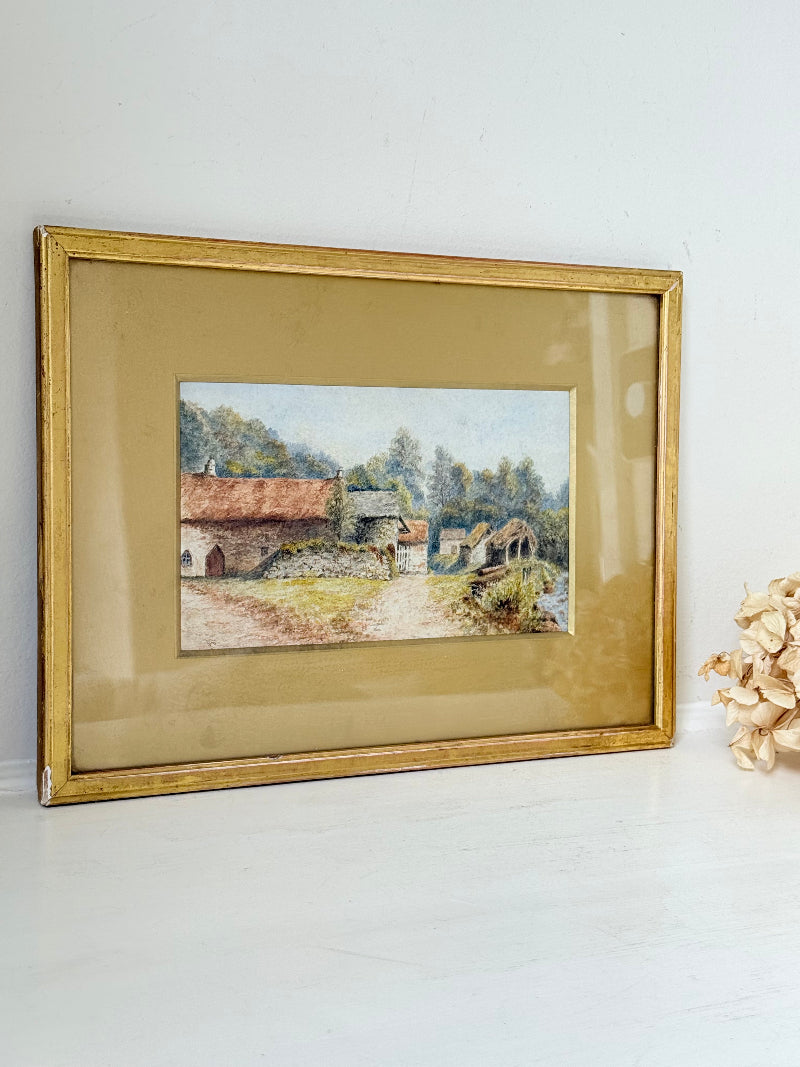 Framed vintage watercolour of countryside farm buildings with red roofs in gold frame photographed on a white surface