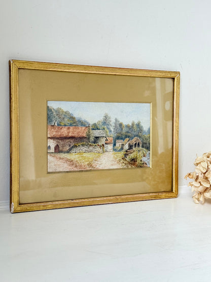 Framed vintage watercolour of countryside farm buildings with red roofs in gold frame photographed on a white surface