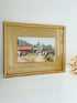 Framed vintage watercolour of countryside farm buildings with red roofs in gold frame photographed on a white surface
