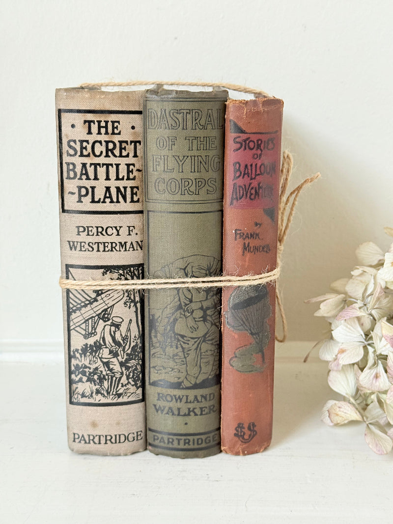 Vintage decorative book bundle in red, olive green and cream tied with twine, photographed on a white surface