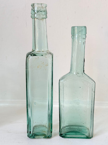 Set of five antique aqua green glass bottles with embossed lettering, photographed on a white surface
