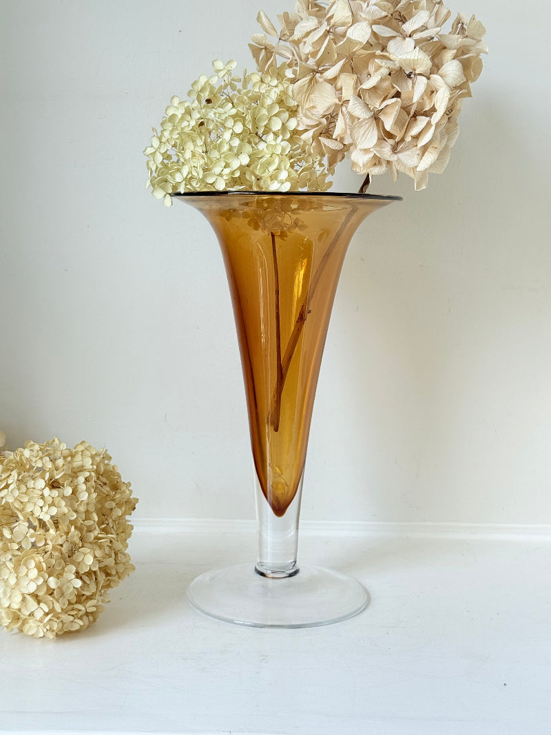 Tall mid-century amber trumpet vase with flared rim and clear glass foot, styled against a neutral background